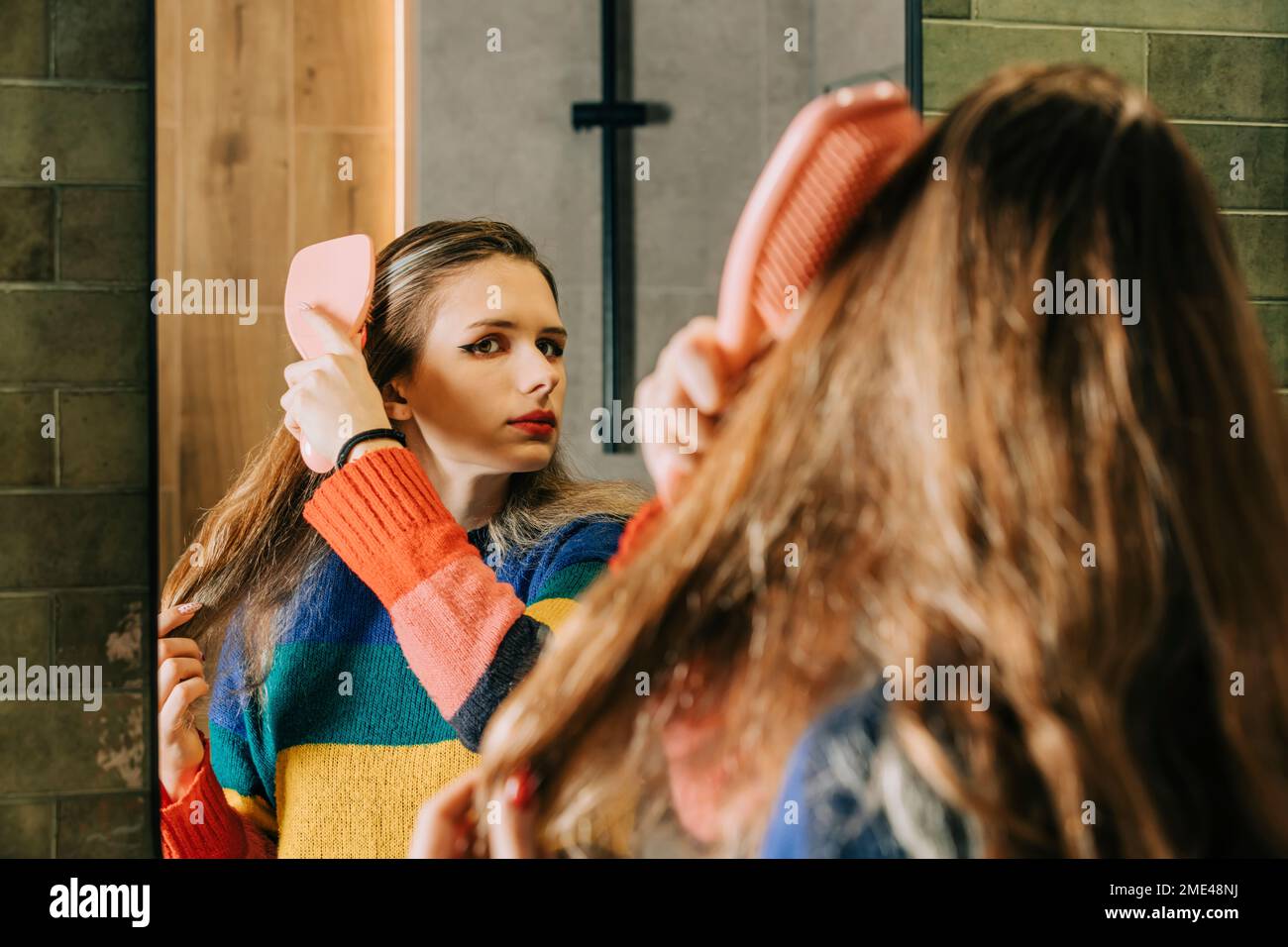Girl brushing hair with comb looking in bathroom mirror Stock Photo