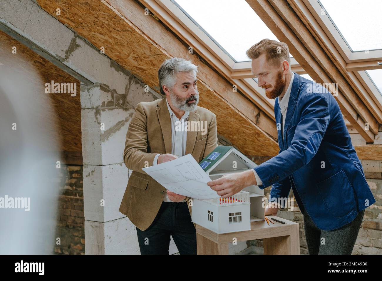 Architect explaining colleague over blueprint standing by house model ...