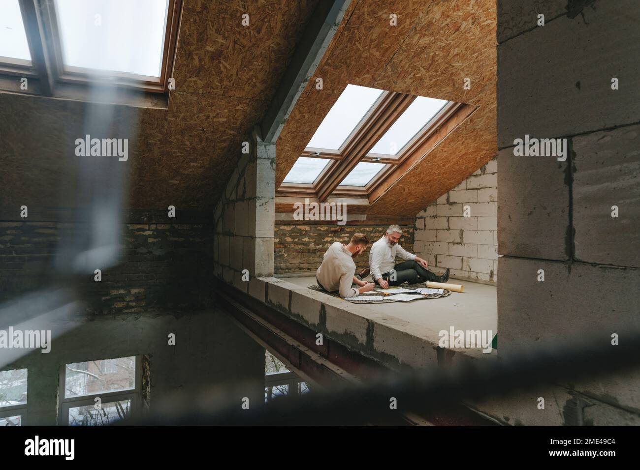 Architects working on blueprint sitting on floor at construction site Stock Photo
