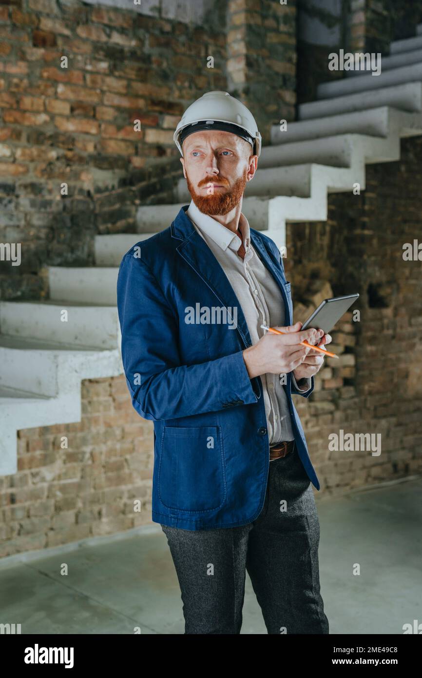 Thoughtful architect standing with tablet PC at under construction site Stock Photo
