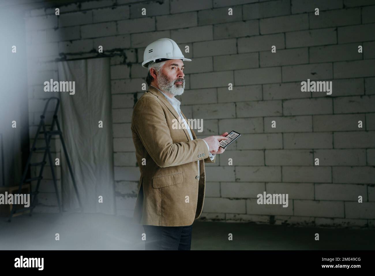 Thoughtful architect standing with tablet PC at construction site Stock Photo