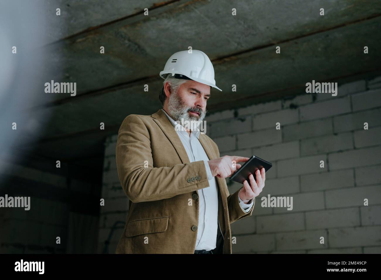 Architect wearing hardhat using tablet PC standing at construction site Stock Photo