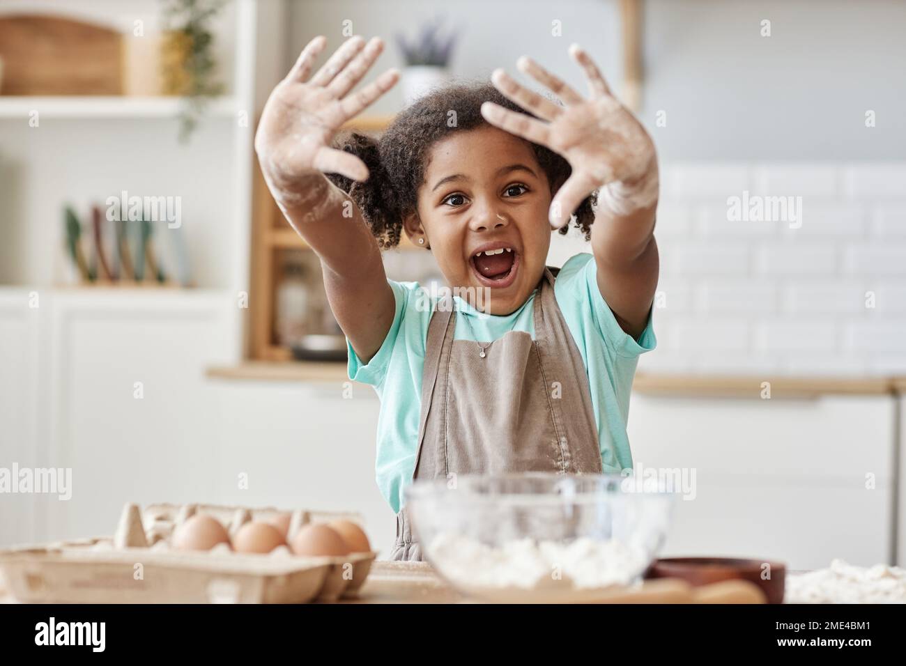 Portrait of happy black girl enjoying baking in kitchen and showing hands with flour to camera, copy space Stock Photo