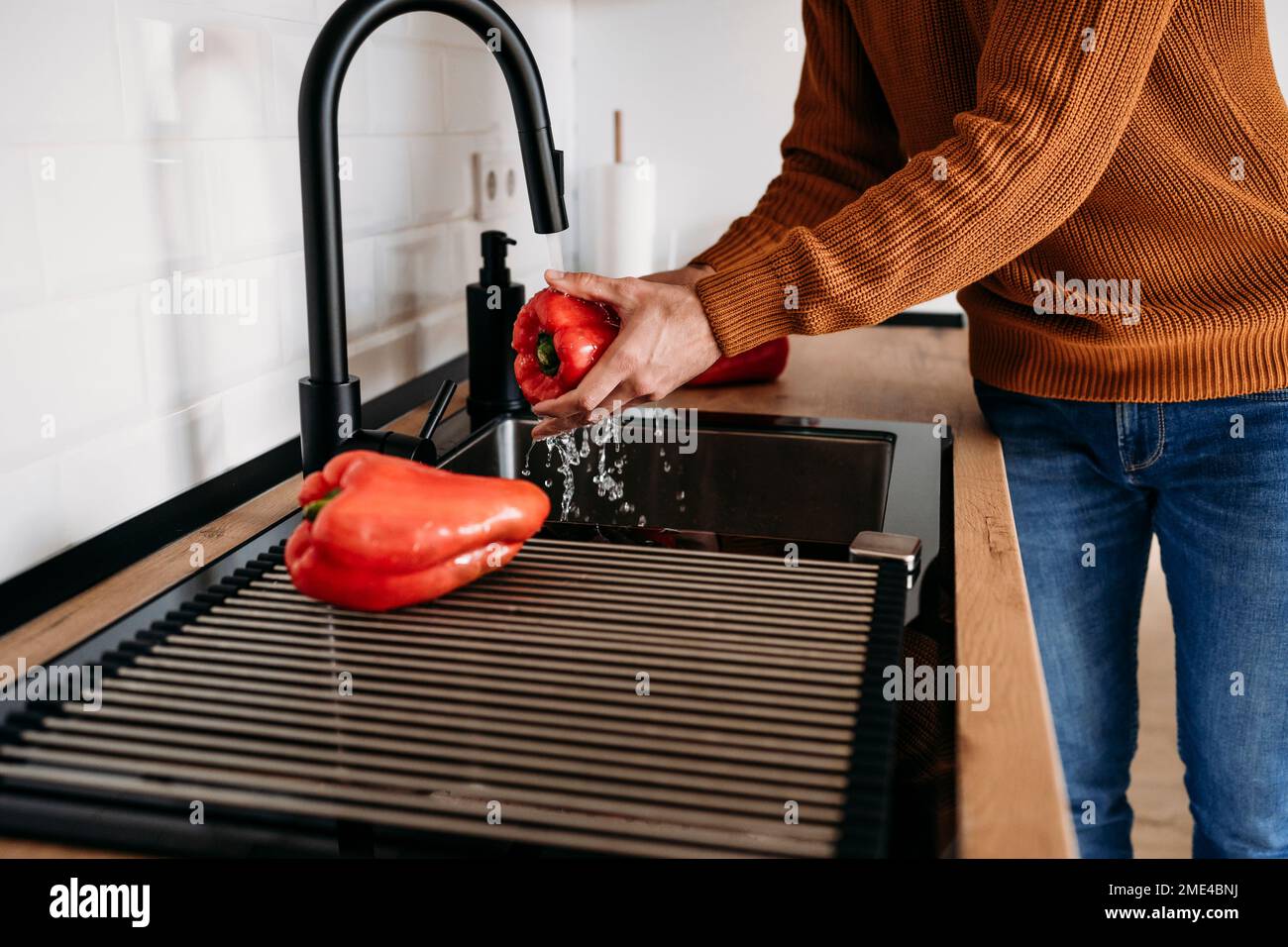 Hands of man washing red bell peppers in sink at home Stock Photo