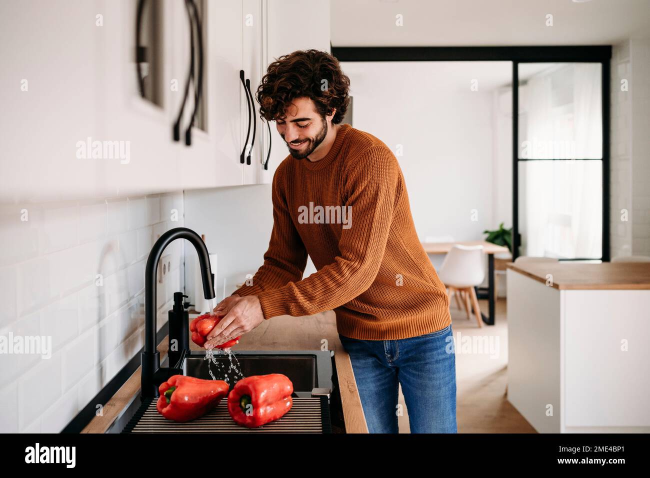 Happy man washing red bell peppers in sink at home Stock Photo