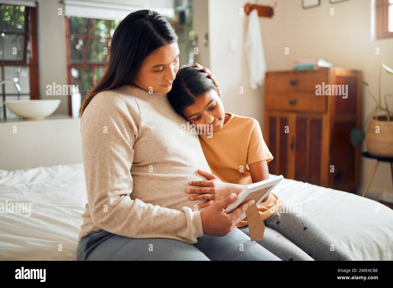 Pregnant mom and child look at a picture frame together in the bedroom
