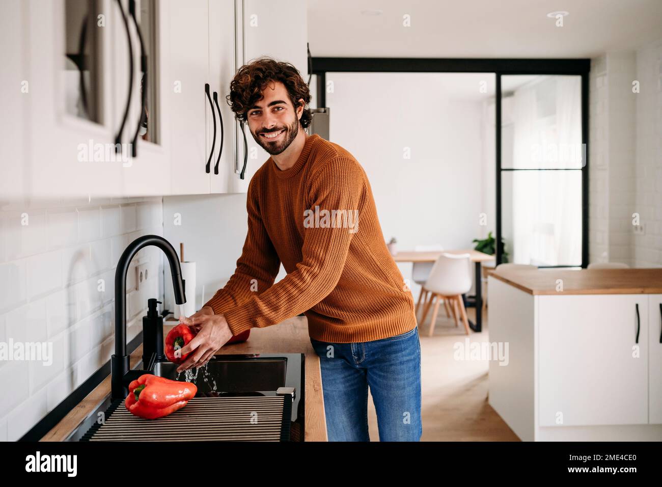 Smiling young man washing red bell pepper at home Stock Photo