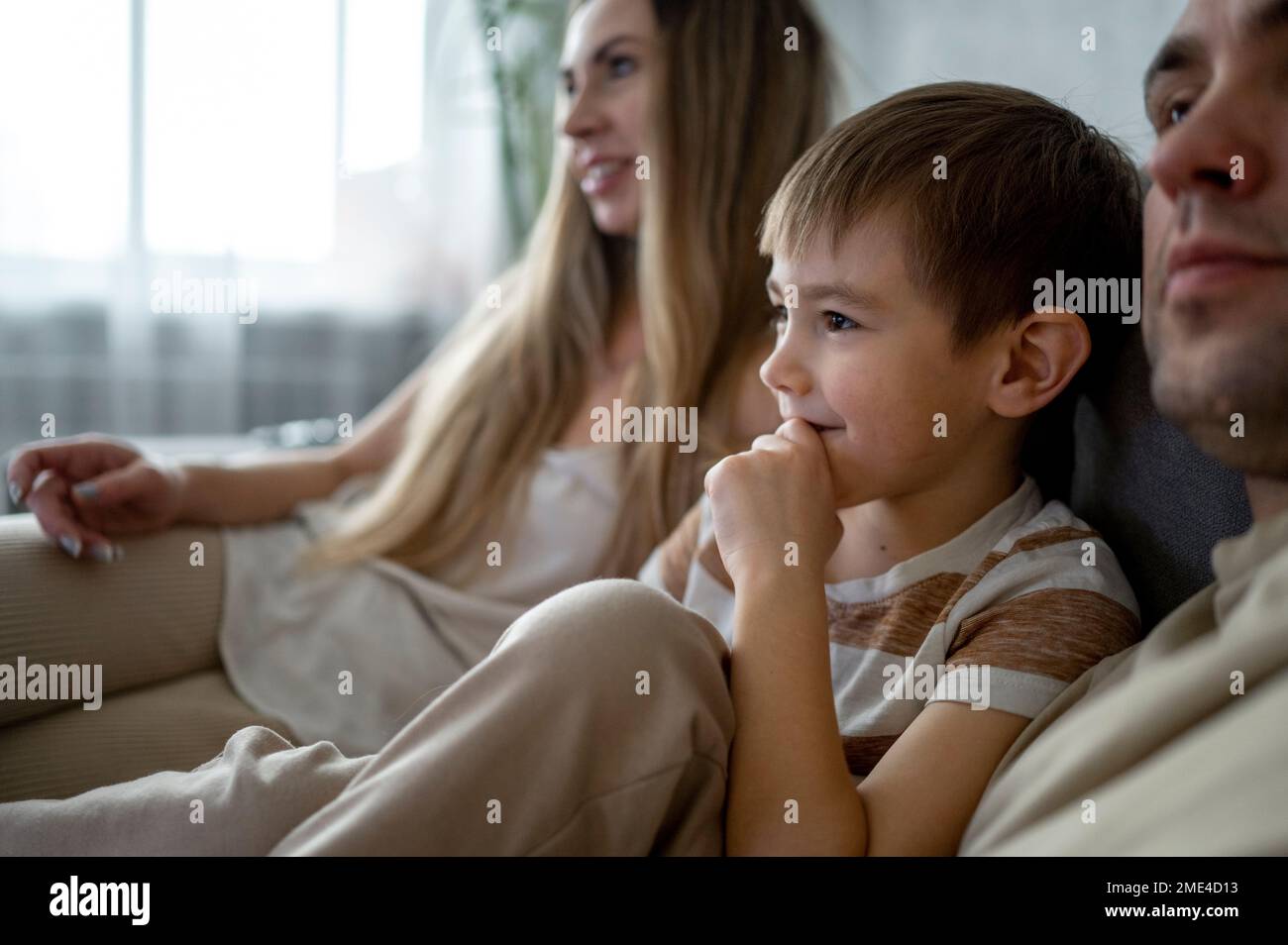 Smiling son spending leisure time with parents on sofa at home Stock Photo