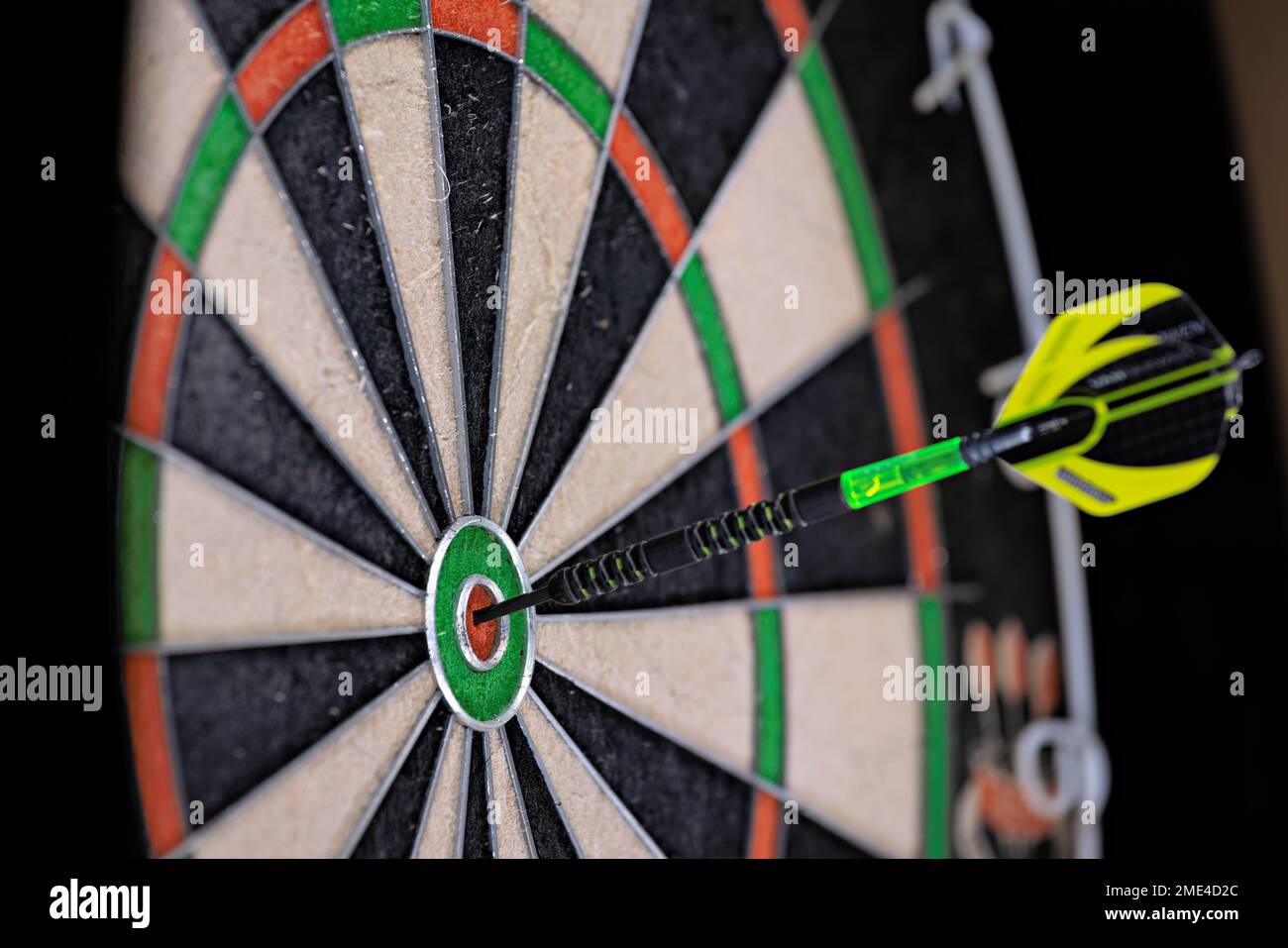 Single black and green dart stuck in the bullseye of a dartboard. Close