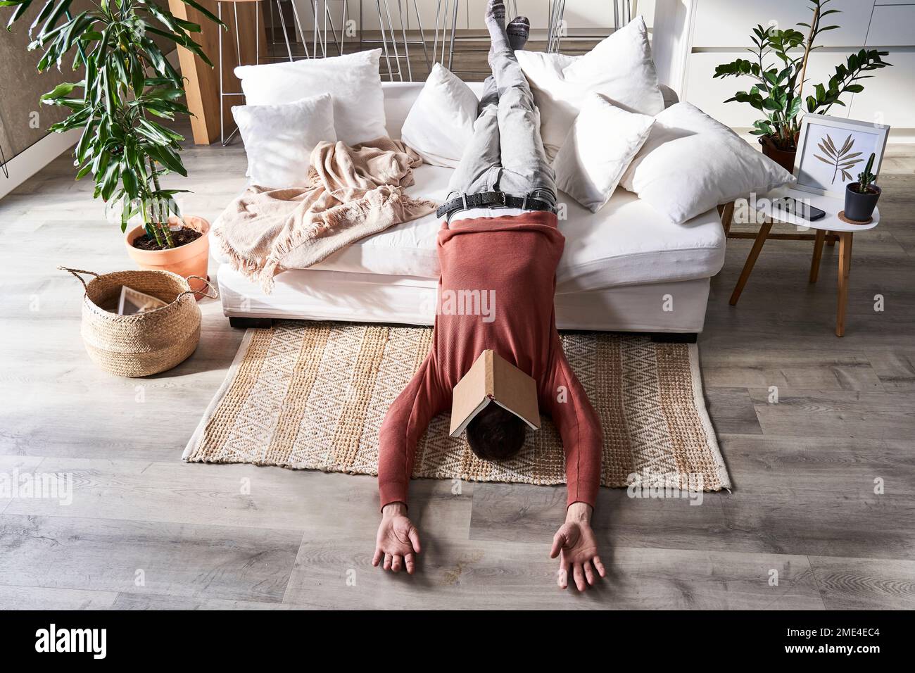 Man with book on face lying upside down at home Stock Photo