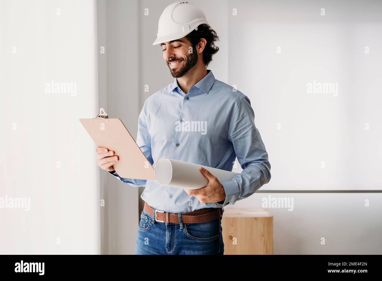 Smiling architect holding blueprints by window in office Stock Photo