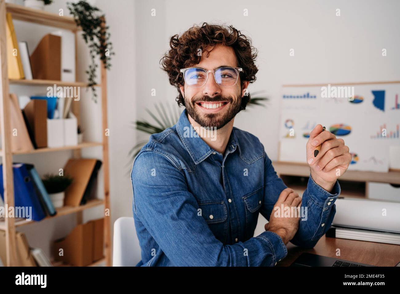 Cheerful young engineer wearing eyeglasses holding pen in office Stock Photo