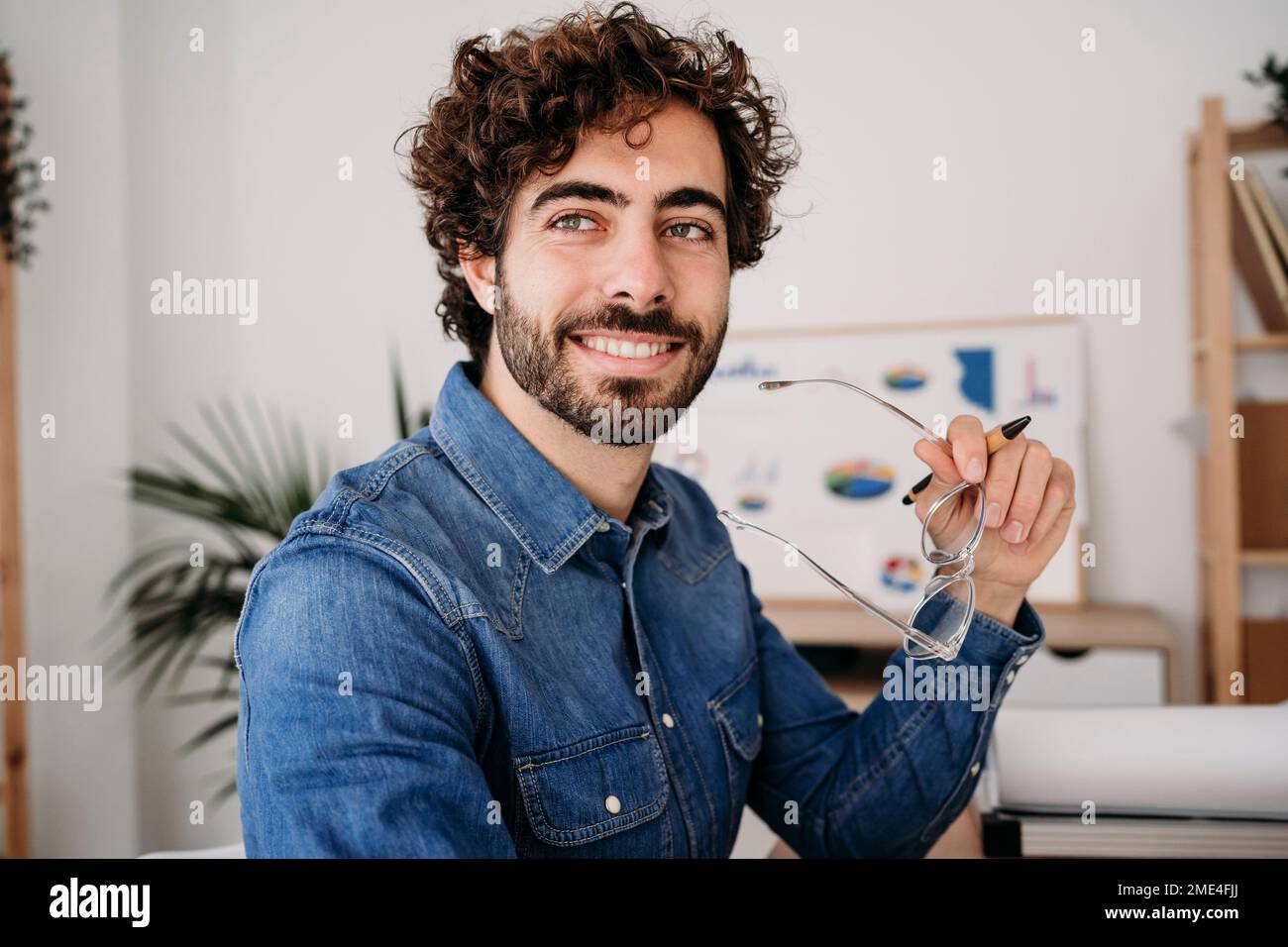 Contemplative young engineer holding eyeglasses in office Stock Photo