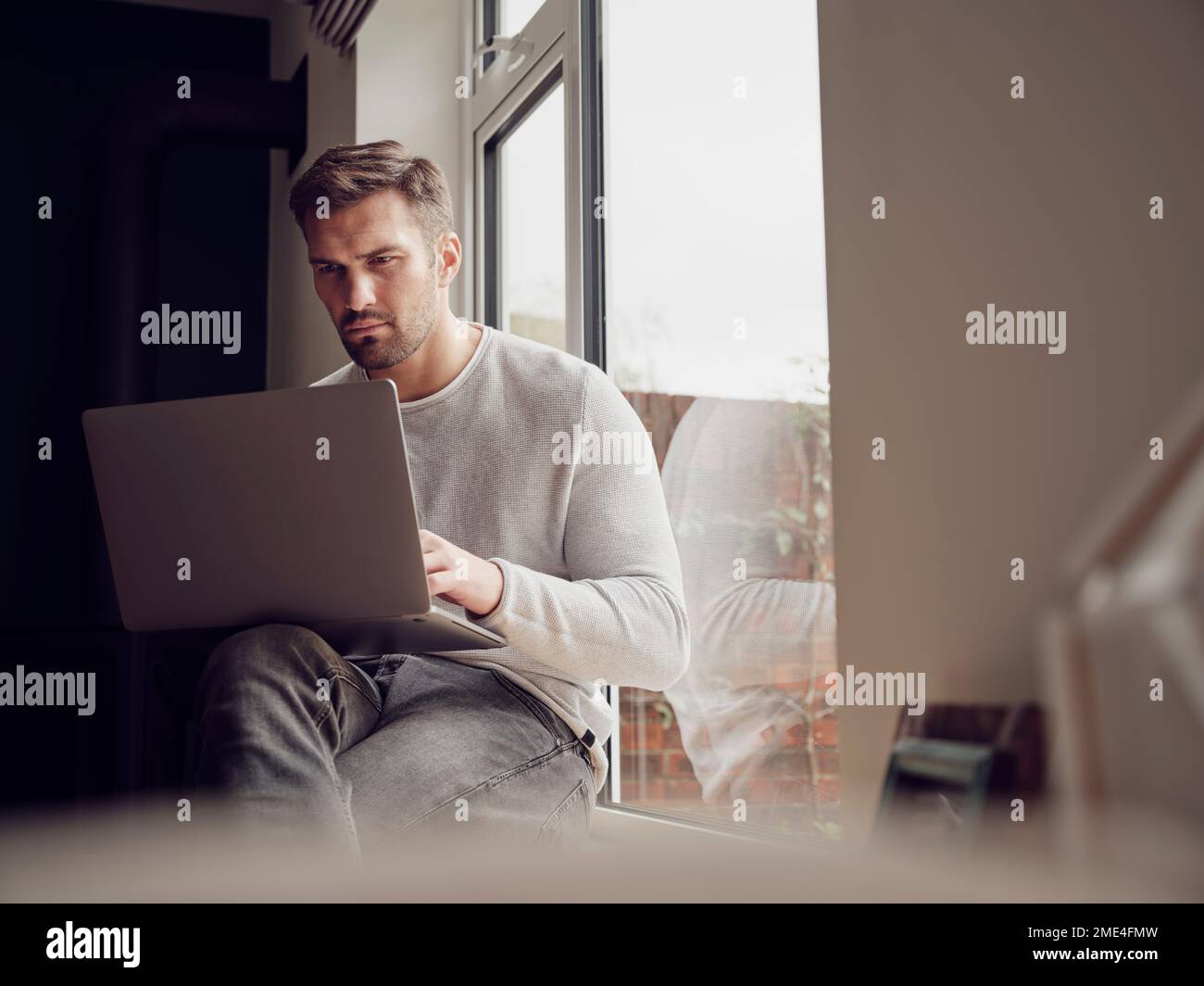 Man by the window at home using laptop Stock Photo