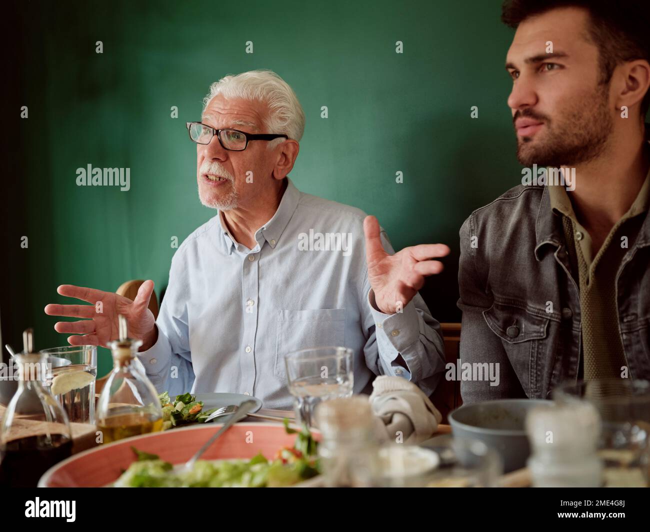 White-haired man sitting awith adukt son at lunch table gesturing Stock Photo