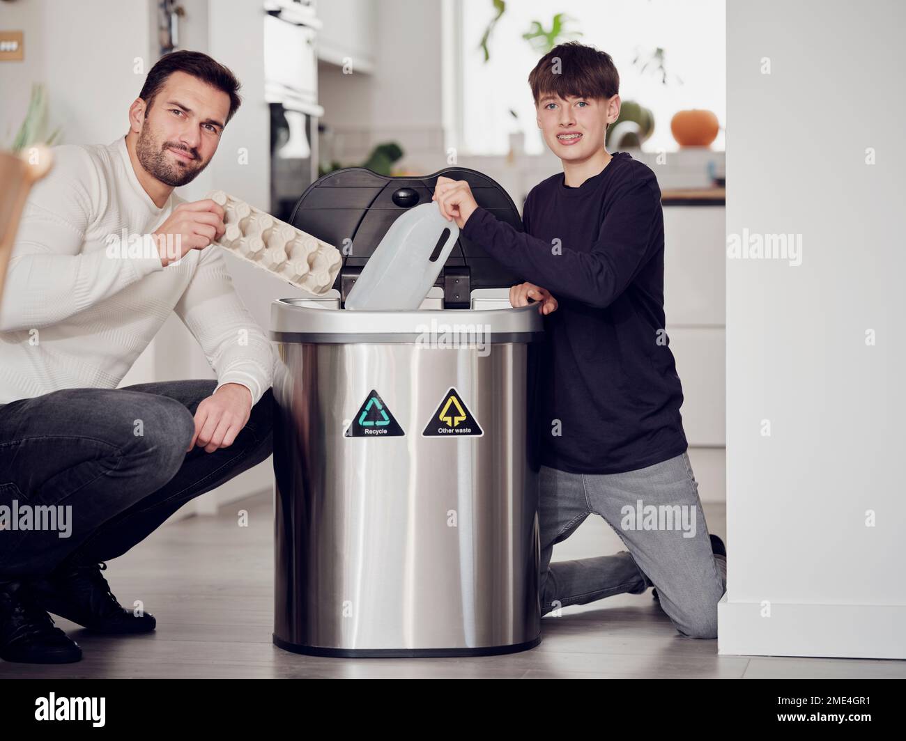 Father and son sorting waste paper and plastic into a sorting bin Stock Photo