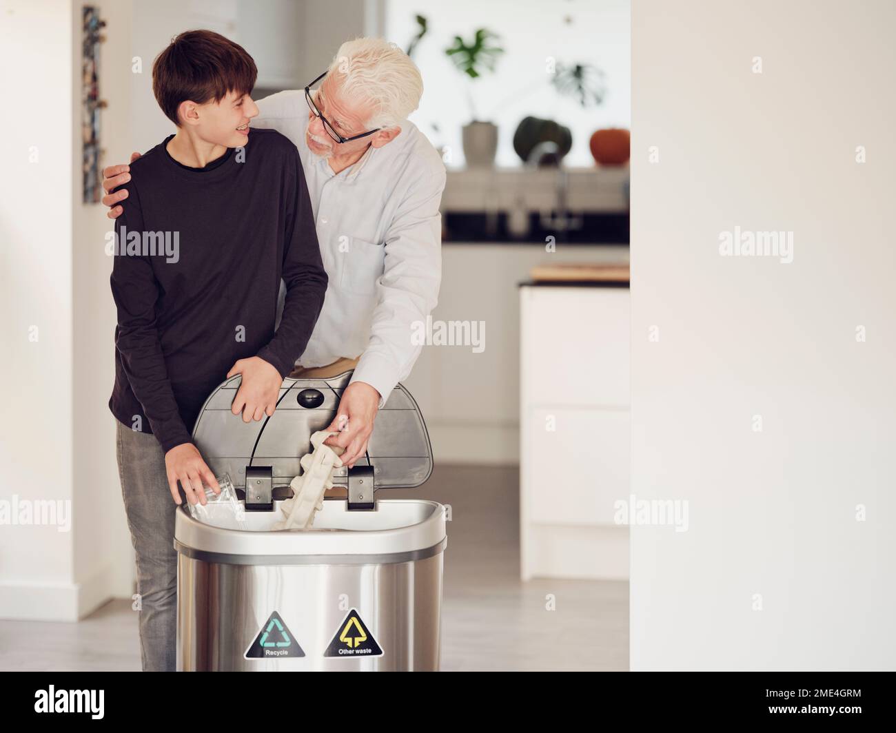 Grandfather and grandson sorting waste paper and plastic into a sorting bin Stock Photo