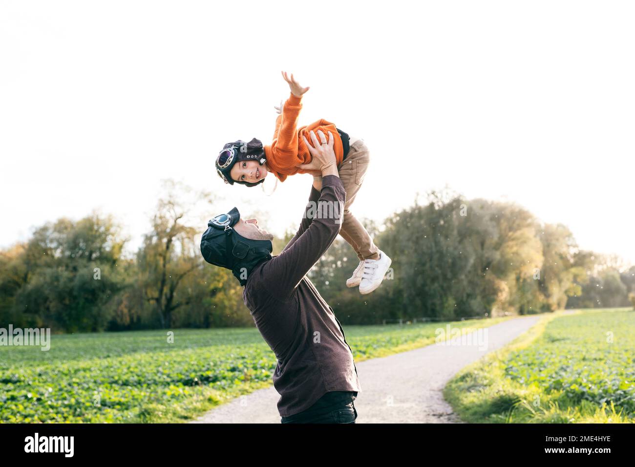 Carefree man lifting son wearing flying goggles in nature Stock Photo