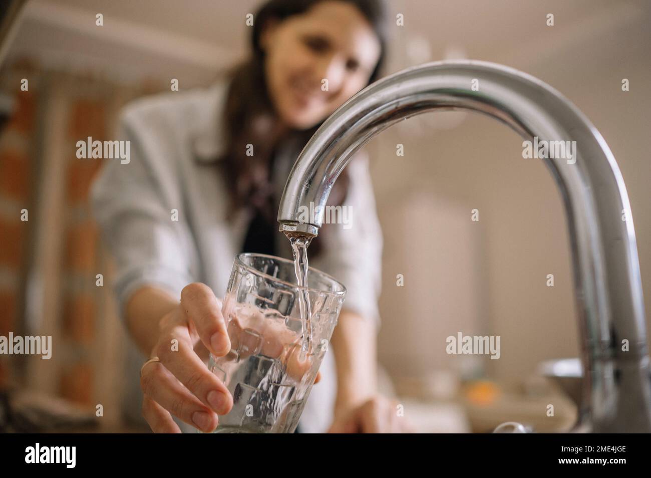 Woman filling water from faucet in glass at home Stock Photo
