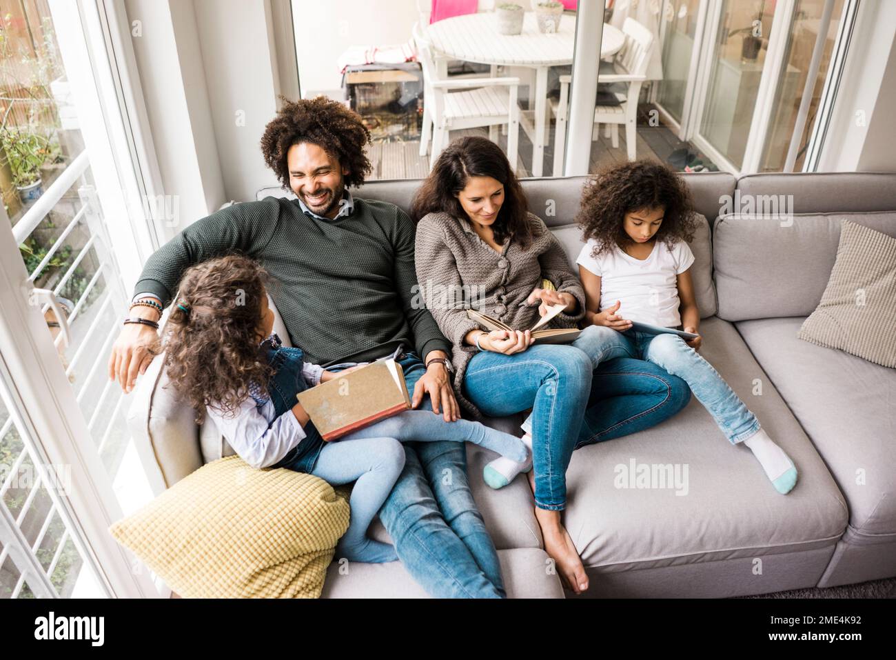 Happy father with mother and daughters reading book on sofa at home Stock Photo