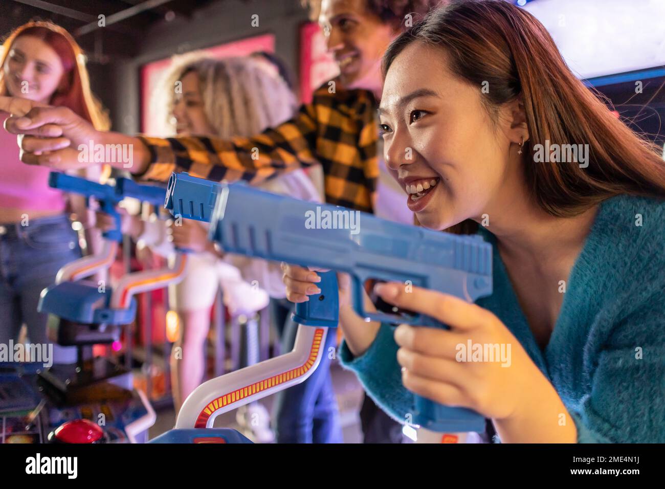 Happy young woman enjoying shooting game with friends at arcade Stock
