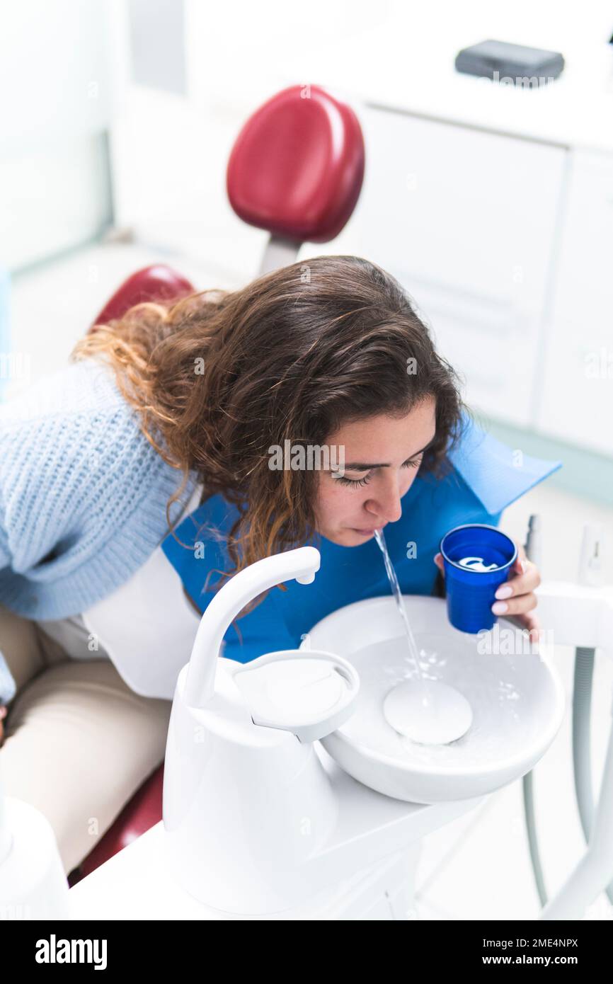 Woman spitting water in sink at dental clinic Stock Photo Alamy