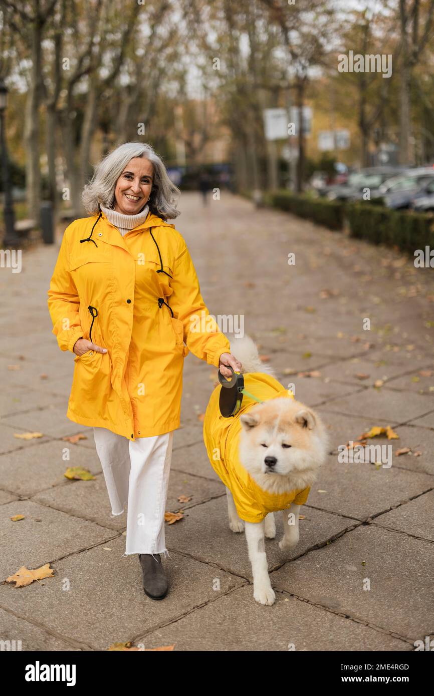 Happy senior woman walking with dog on footpath Stock Photo