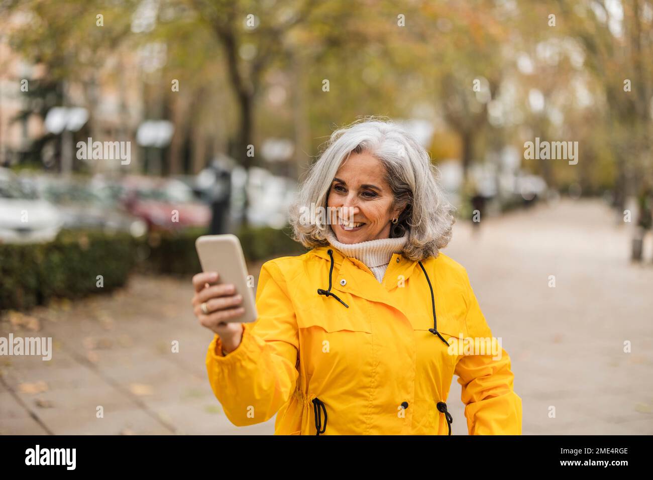 Happy senior woman using smart phone at footpath Stock Photo