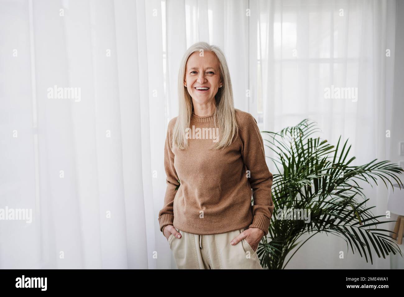Happy mature woman with hands in pockets standing at home Stock Photo ...