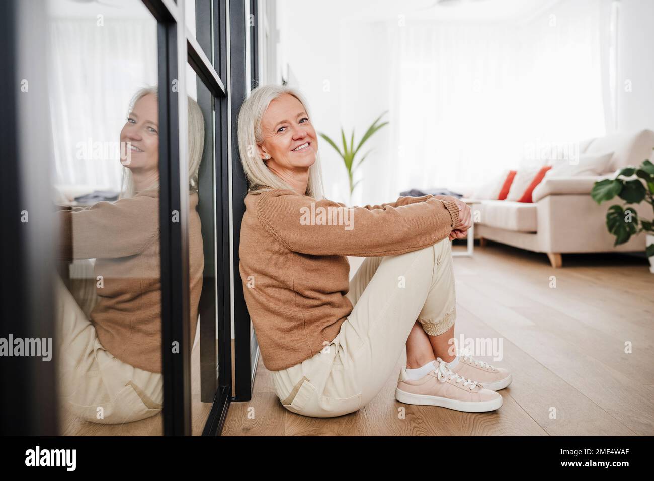 Happy woman sitting on floor in living room Stock Photo - Alamy