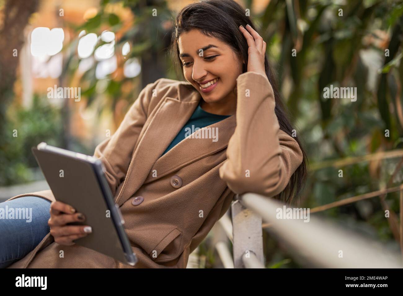 Happy woman using tablet PC sitting by railing Stock Photo