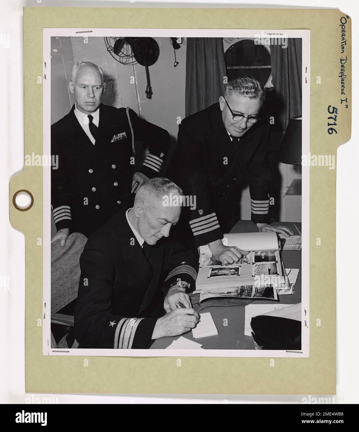 Operation Defense I. Captain Oscar Carl Rohnke, USCG Commanding Officer, Coast Guard Icebreaker Eastwind, receives an autograph for his scrapbook from Rear Admiral Richard E. Byrd, USN (Ret), Head of U. S. Antarctic Programs, and veteran of four previous Antarctic expeditions. Watching (left) is Captain Carlos W. Thomas, USCG, who as a result of his knowledge and five years' Arctic experience and Antarctic experience on the 1946-1947 expedition as commanding officer of the Coast Guard Icebreaker Northwind, was assigned to duty under the Chief of Naval Operations as Chief of Staff for Commander Stock Photo