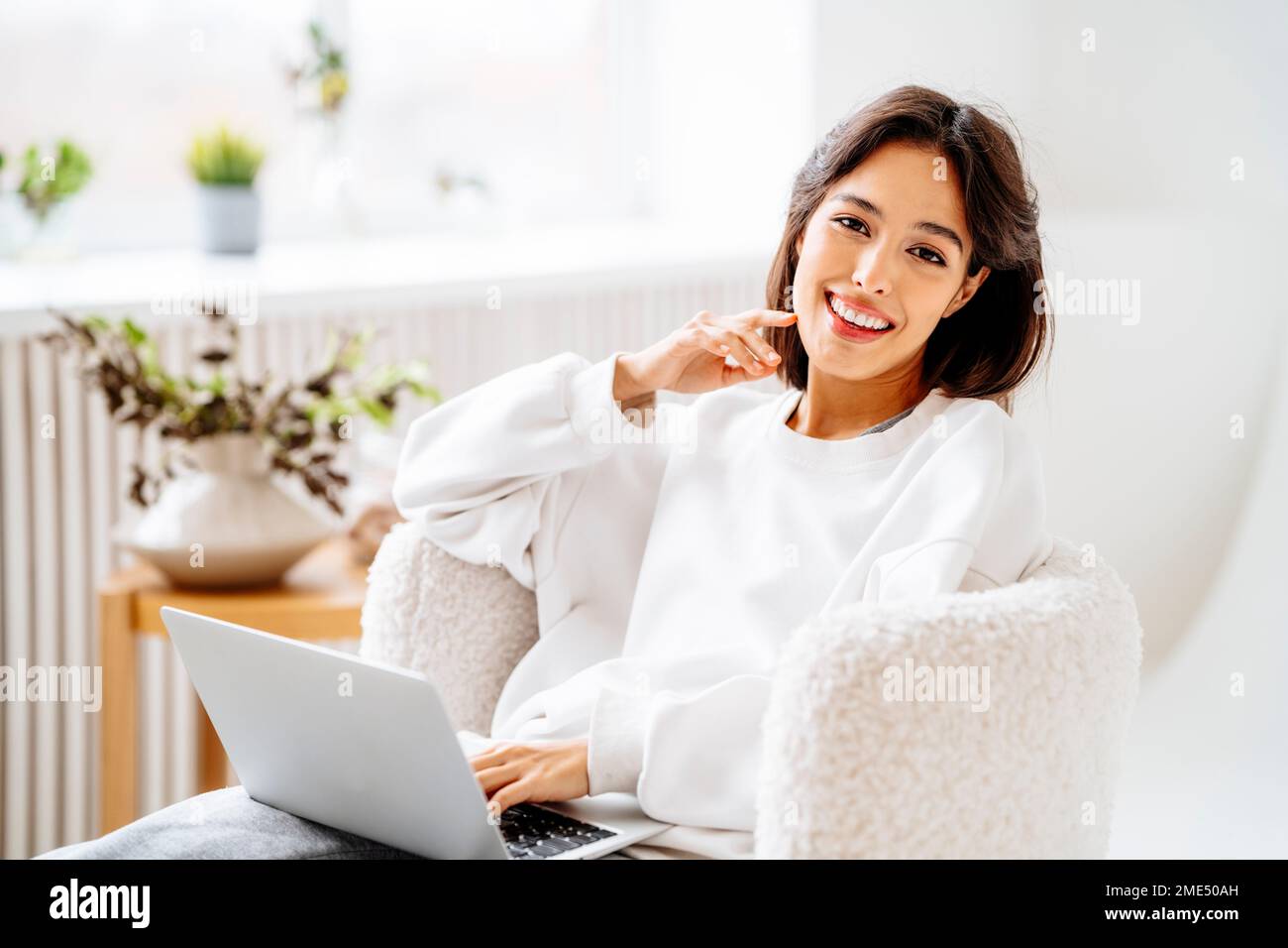 Happy young woman with laptop sitting on chair Stock Photo - Alamy