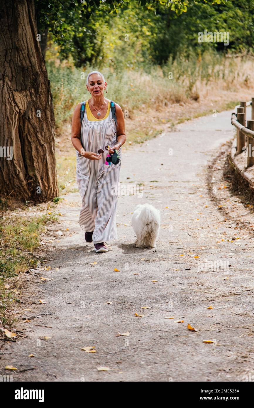Senior woman walking with dog on footpath at park Stock Photo