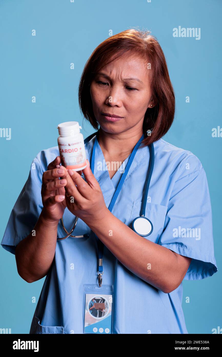 Serious medical assistant working at medication treatment to prevent patient sickness, holding drugs box reading pharmaceutical leaflet in studio with blue background. Health care service and concept Stock Photo