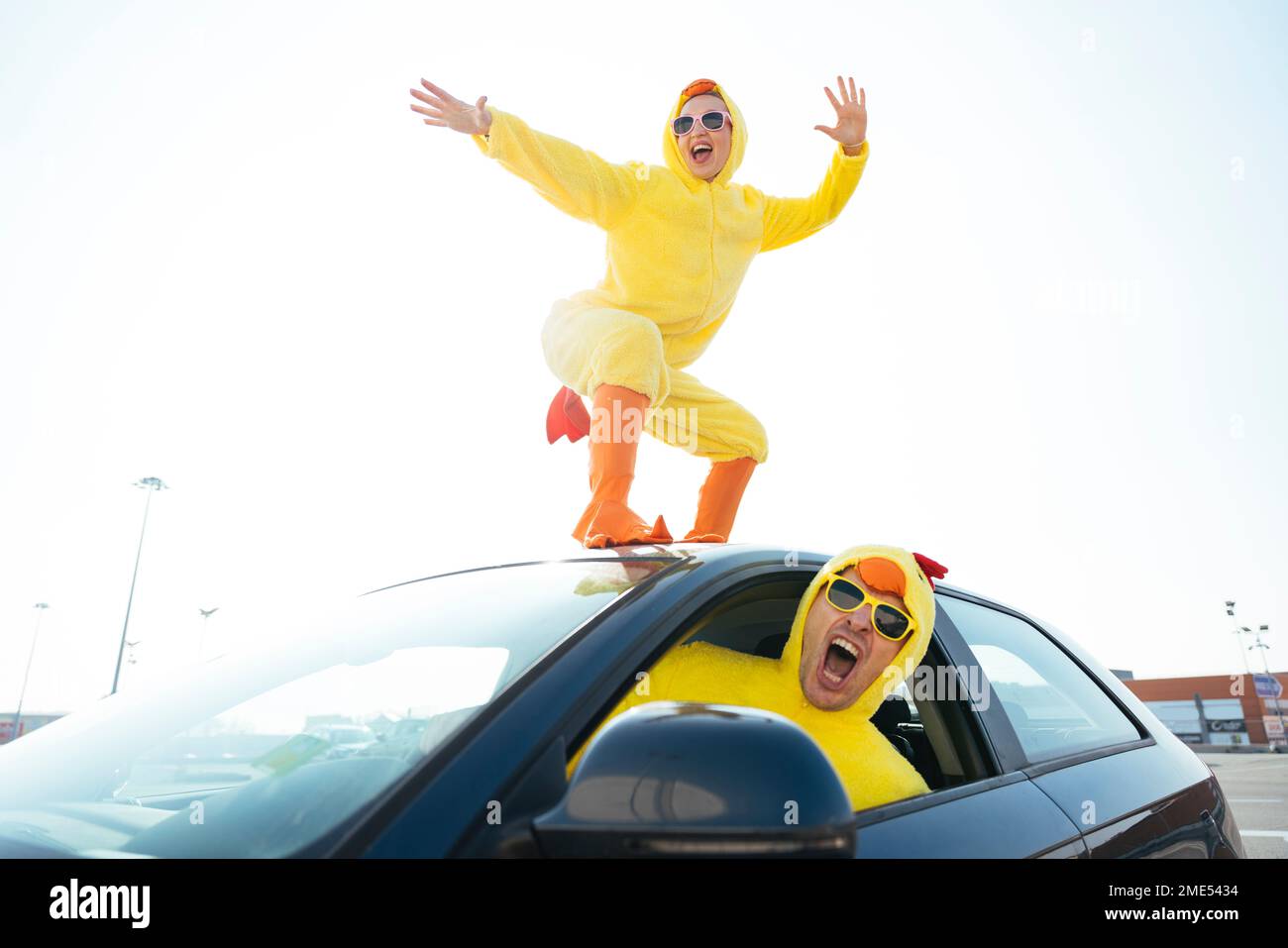 Man screaming and driving car with carefree woman in chicken costume dancing on roof Stock Photo