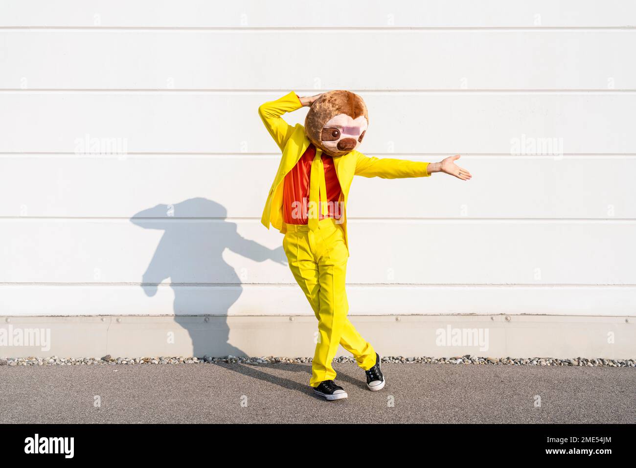 Man wearing animal mask dancing in front of wall on sunny day Stock Photo