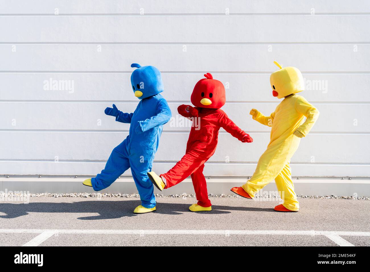 Woman with friends wearing duck costumes dancing in front of white wall Stock Photo