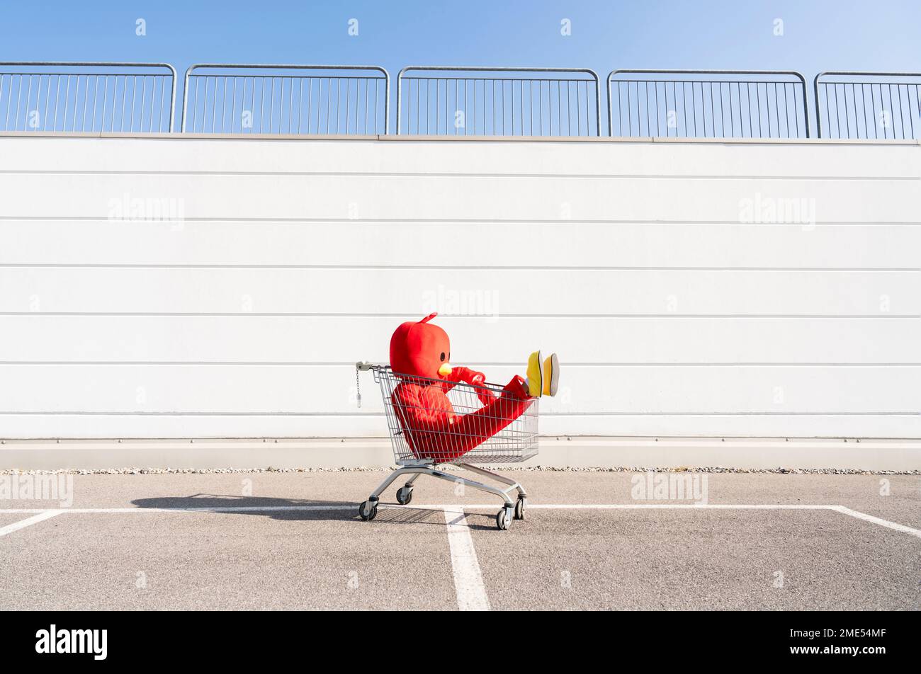 Woman wearing red duck costume sitting in shopping cart Stock Photo