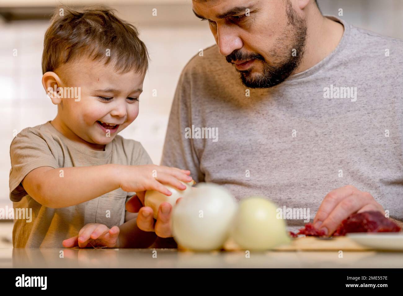 Happy boy taking white onion from father in kitchen at home Stock Photo