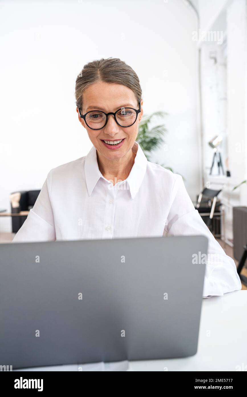Happy businesswoman wearing eyeglasses using laptop in office Stock Photo
