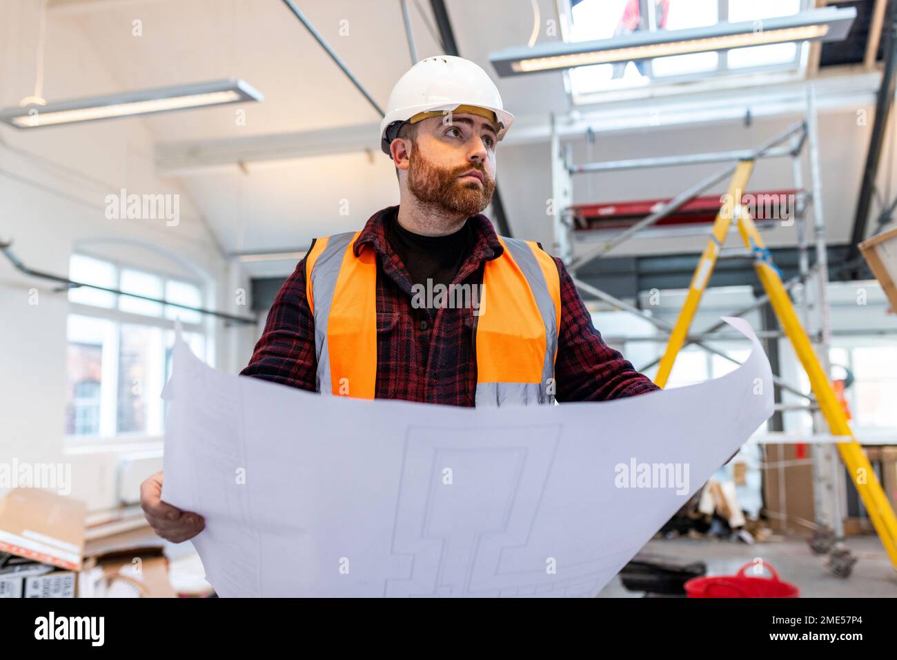 Young engineer standing with blueprint at construction site Stock Photo