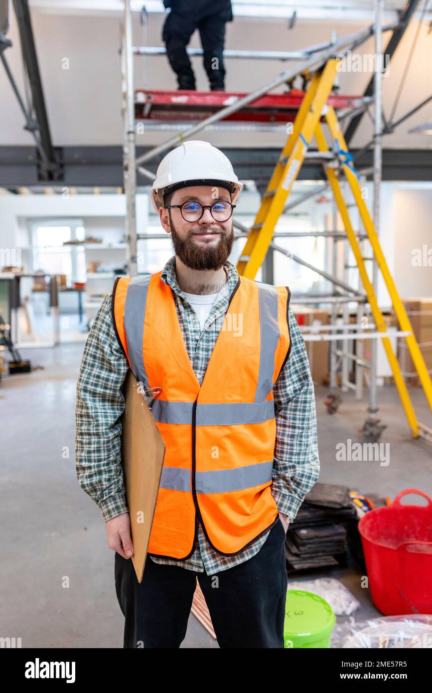 Smiling young engineer holding clipboard standing at construction site Stock Photo