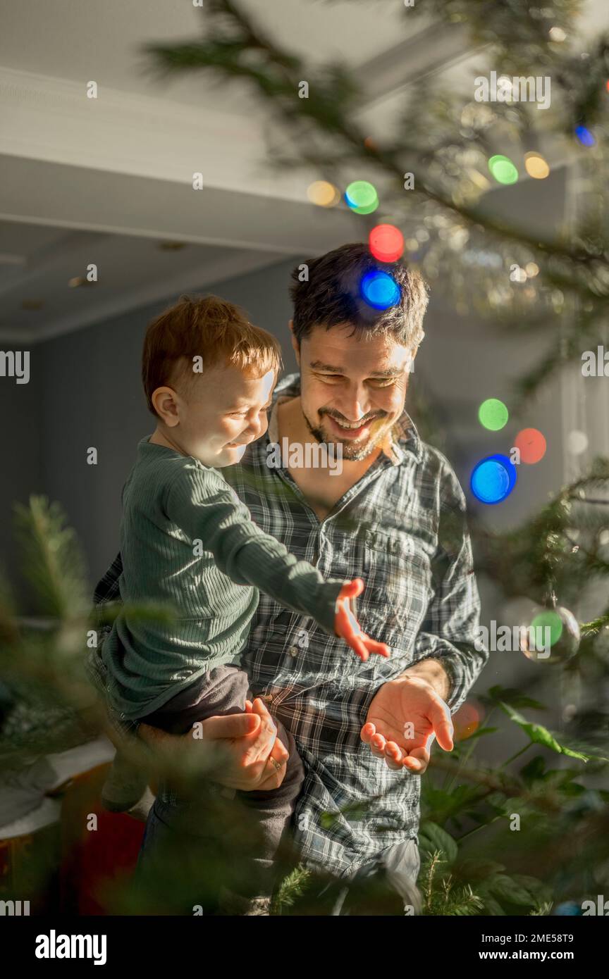 Happy father and son standing in front of Christmas tree at home Stock Photo