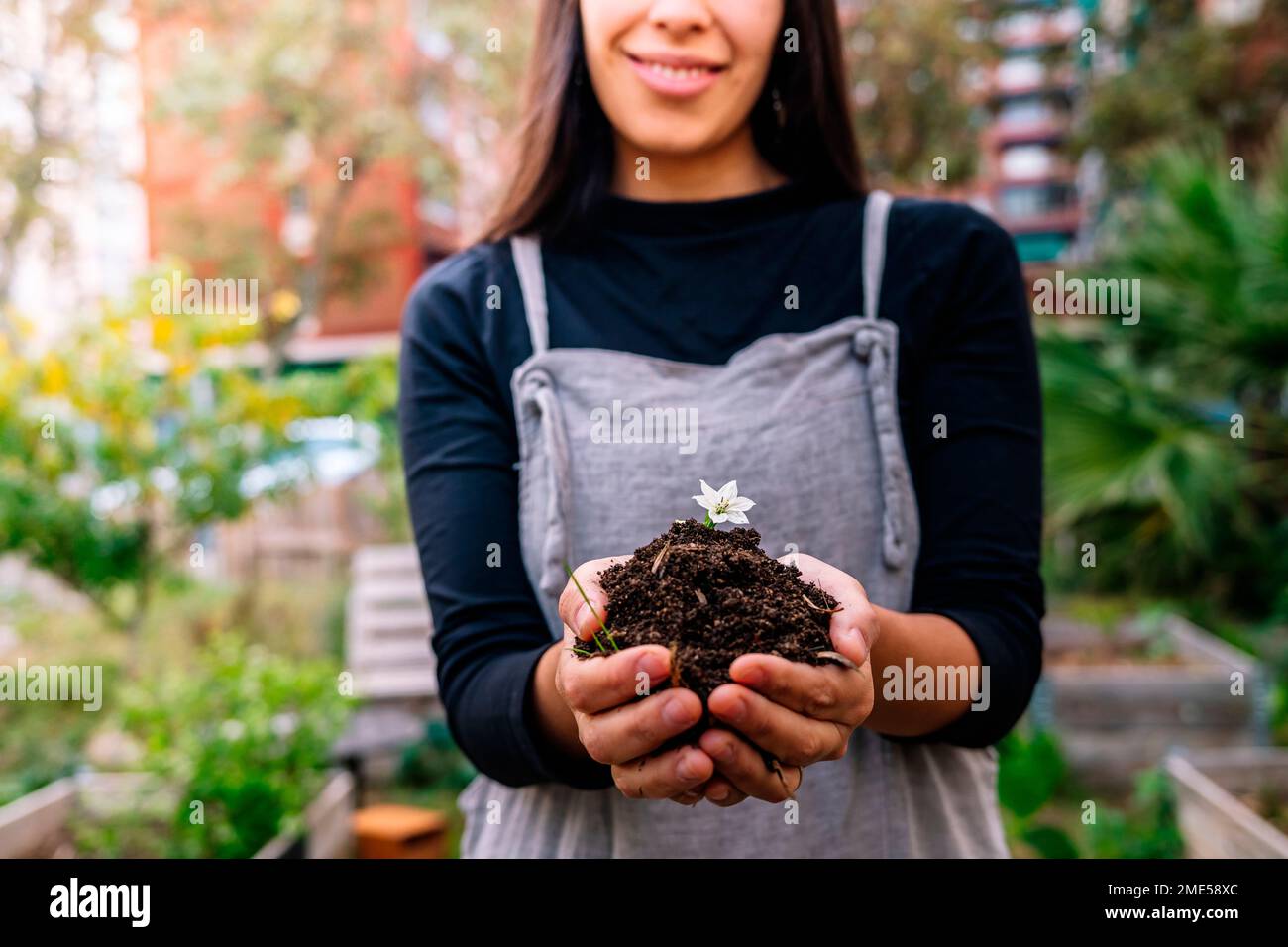 Smiling woman holding dirt with small flower in cupped hands Stock Photo