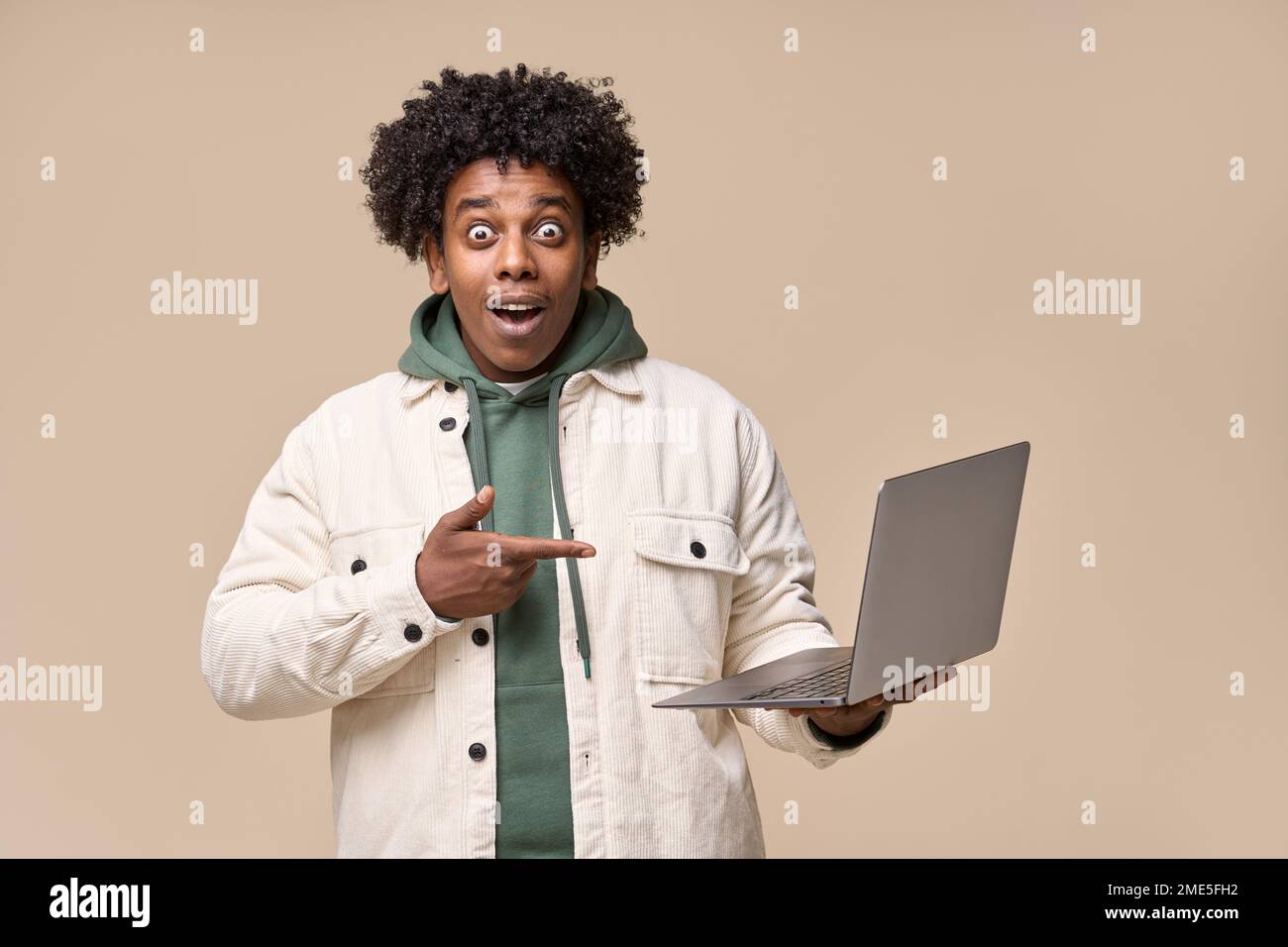 Surprised African guy holding laptop pointing at computer advertising wow offer. Stock Photo