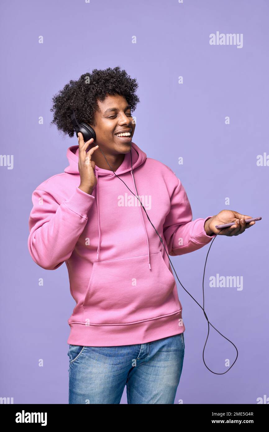 Happy African teen wearing headphones holding cell dancing listening music. Stock Photo