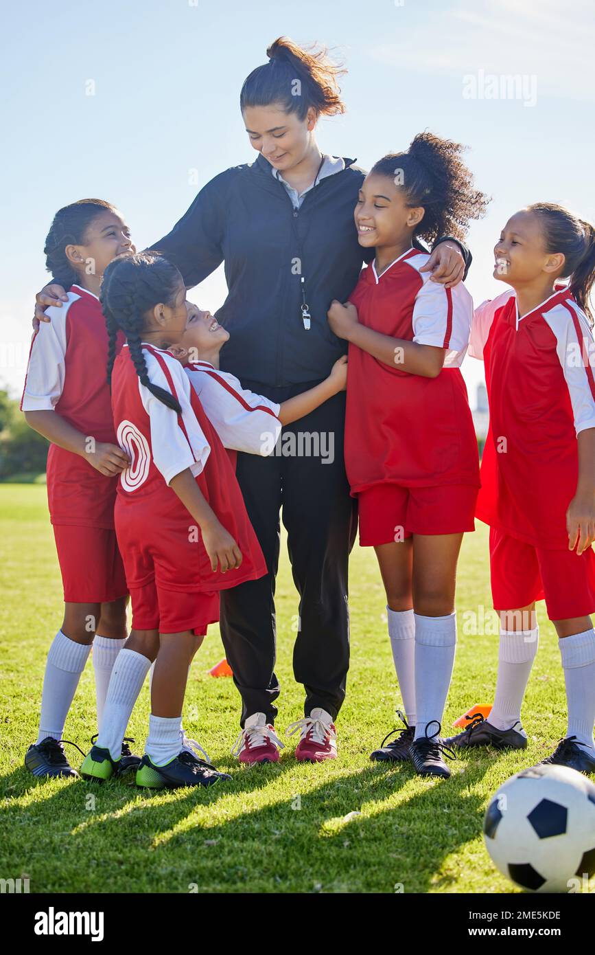 Soccer, girl group hug and coach with happiness, smile or team building, diversity and solidarity on grass pitch. Young female kids, football coaching Stock Photo