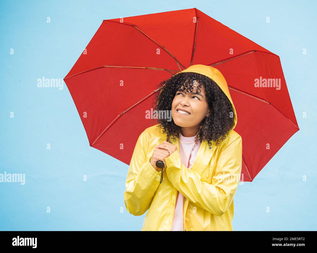 Young african woman, umbrella and wall with smile, rain and fashion raincoat for safety, wellness or protection. Thinking gen z girl, winter or check Stock Photo
