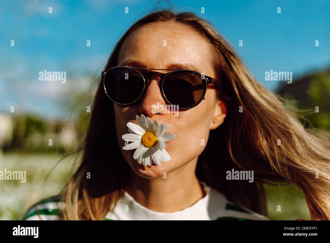 Portrait of a long-haired woman with hair fluttering in the wind and a daisy in her shirts Stock Photo